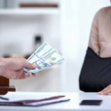 Image of one person handing cash to another in an office setting