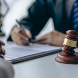 Image of a man in a suit signing paperwork next to a gavel